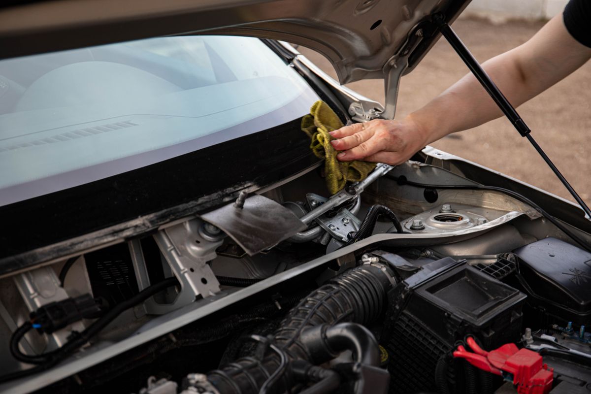 A detailer wiping down a car's windshield and engine area, for illustration